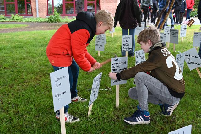 Twee kinderen plaatsen bordjes in de grond als onderdeel van het Kunstwerk van programma Wiede Wold.