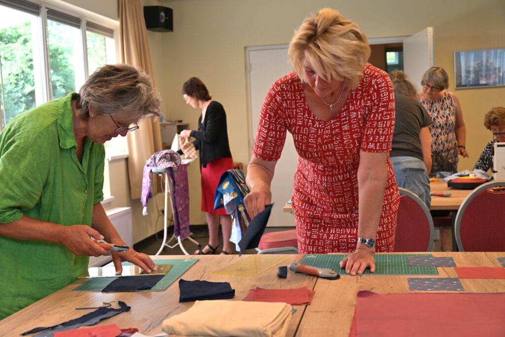 Twee dames zijn lapjes stof aan het snijden voor de patchwork vlag voor de Afvalkathedraal van Wiede Wold. 